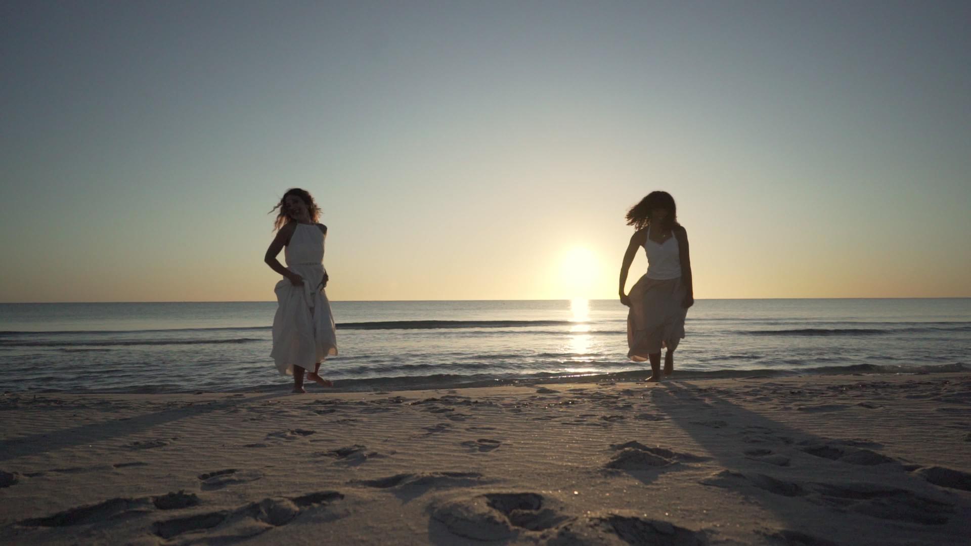 两个多种族的女性朋友从岸边快乐地地从岸边跑到相机或在日落时跑到相机视频的预览图