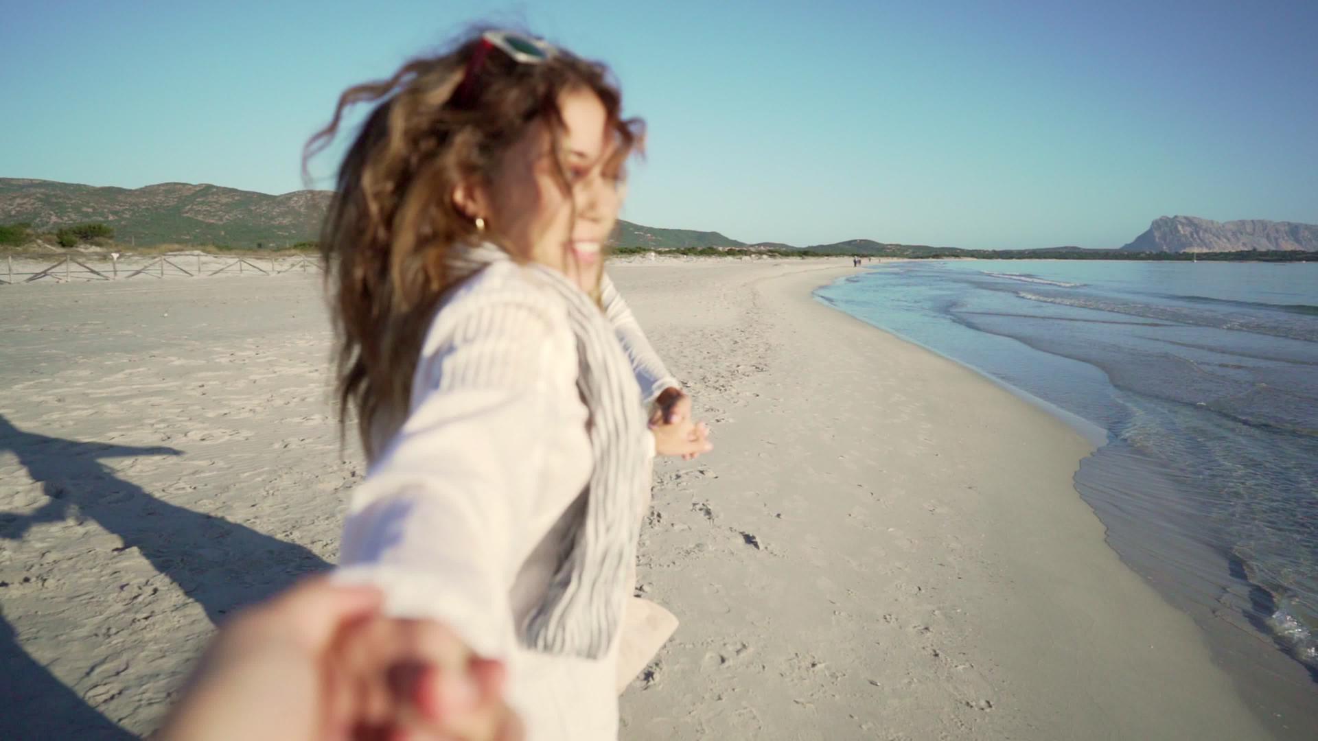 可爱的金发女友在日落或黎明时牵着男人的手和黑人在海滩上视频的预览图