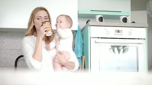 母亲在厨房里喝着咖啡抱着婴儿视频的预览图