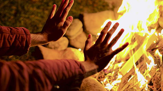 在一个寒冷的秋夜年轻人在营火中温暖了他的手视频的预览图