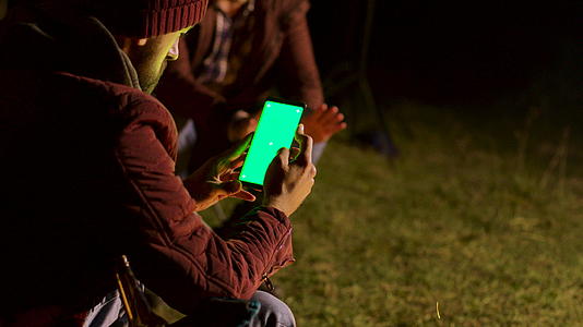 游客在营地火灾周围用绿屏和绿屏扫荡电话视频的预览图