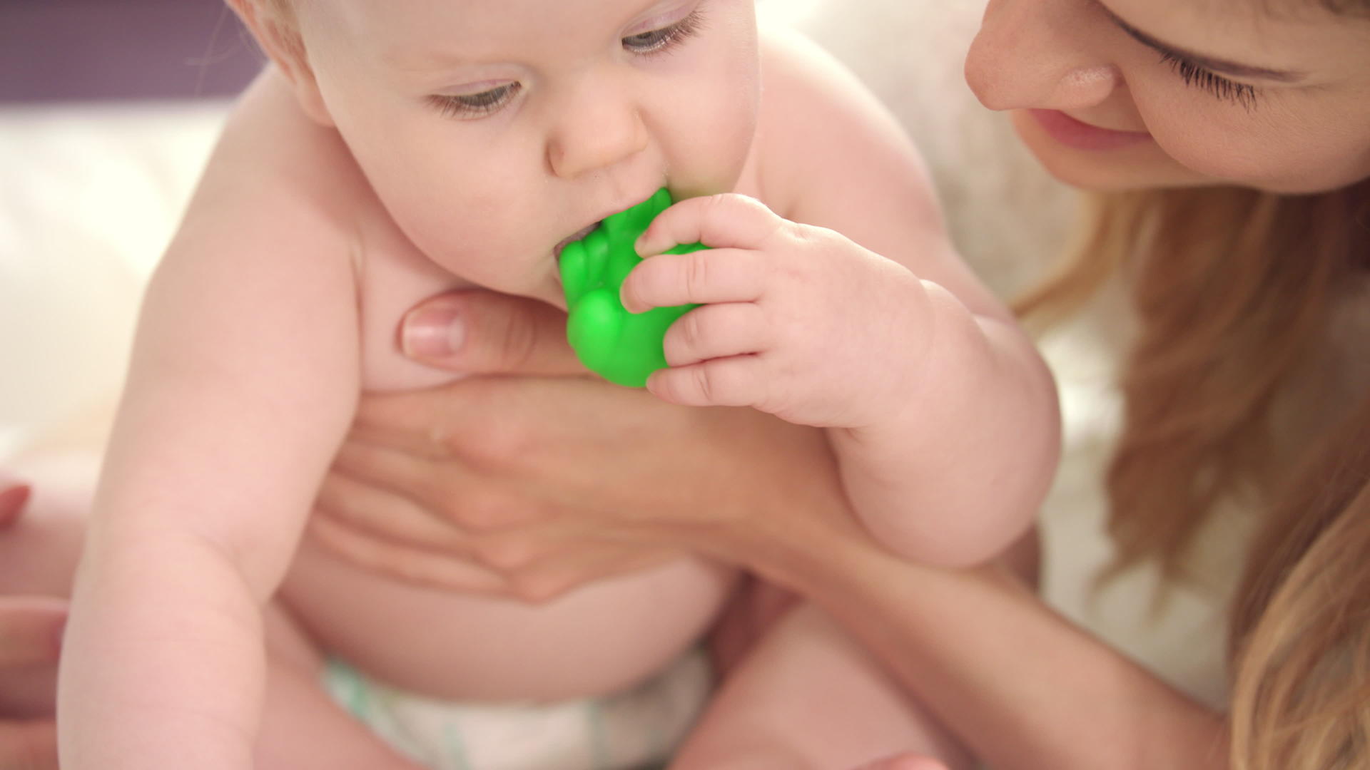 婴儿坐在母亲的怀里戴着尿布玩绿色玩具视频的预览图