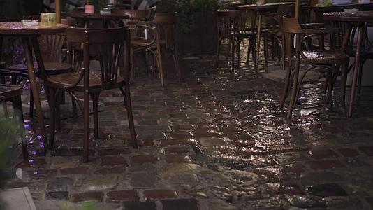 晚上雨中的老街咖啡馆木制家具桌椅在潮湿的鹅卵石上视频的预览图