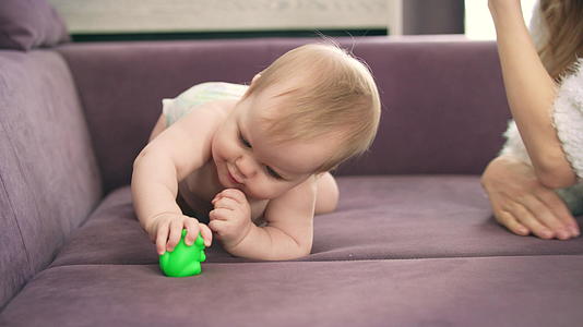 可爱的婴儿爬上紫罗兰的床裸体的孩子穿着尿布咬玩具视频的预览图