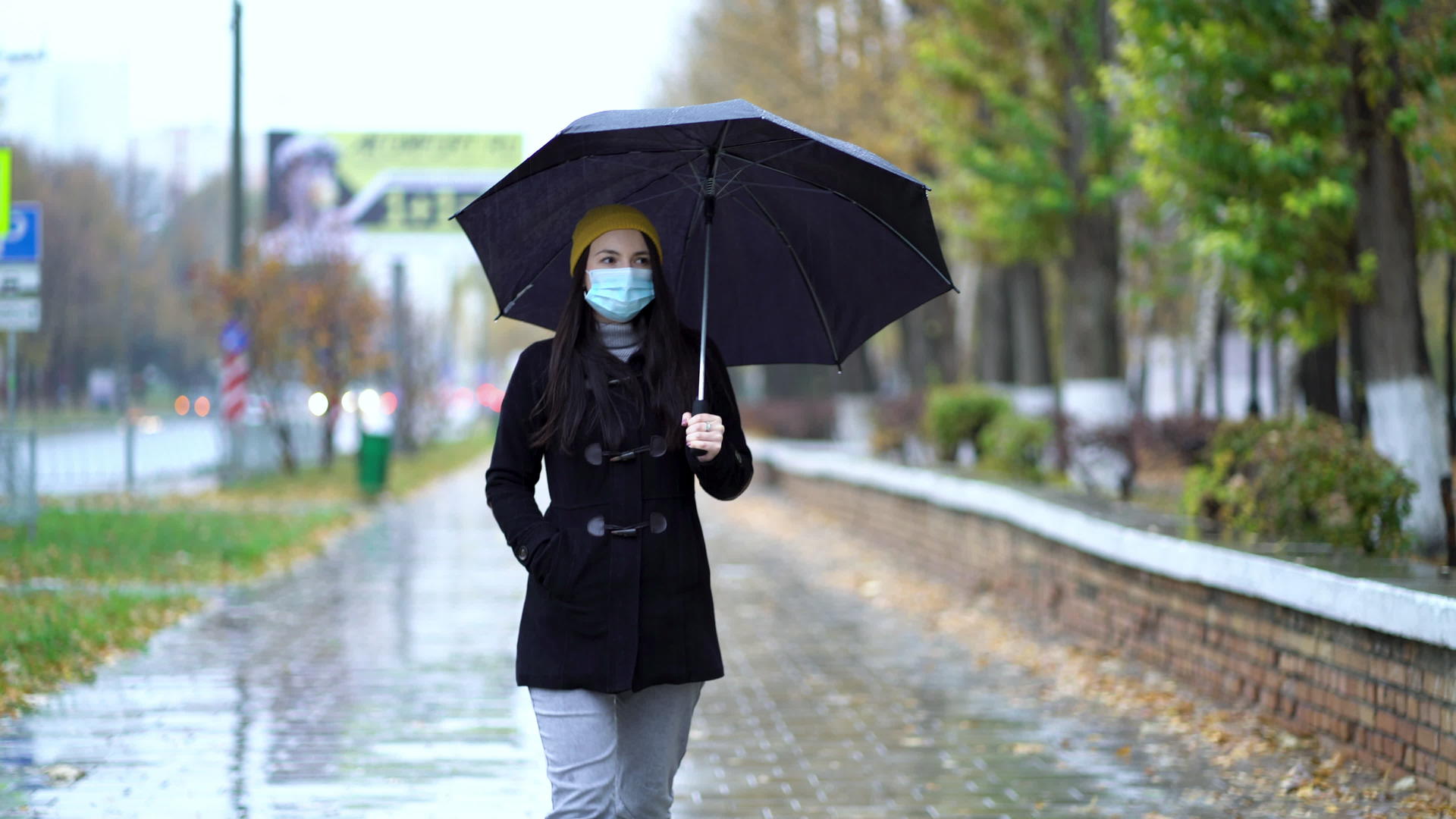 一个戴着防护面具的年轻女子在雨伞下在公园里散步视频的预览图