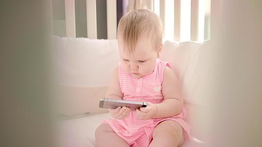 婴儿和智能手机玩游戏的小女孩在上面看卡通视频的预览图
