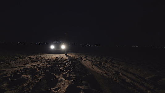 在车头灯前的海滩上奔跑的人的脚影视频的预览图