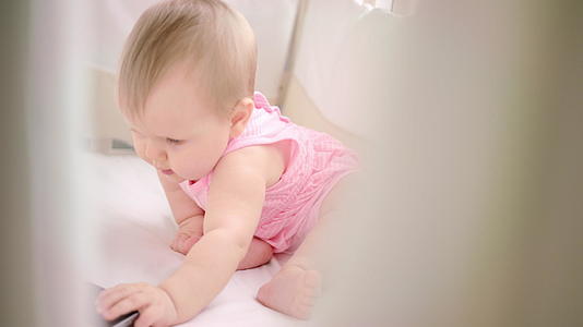 女婴坐在婴儿床上用手机看儿童动画片视频的预览图