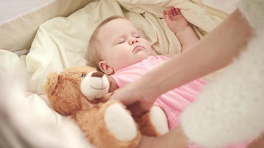 妈妈把玩具放在可爱的婴儿睡觉的床上视频的预览图