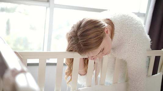 快乐的母亲看着睡在婴儿床附近婴儿床里的孩子视频的预览图