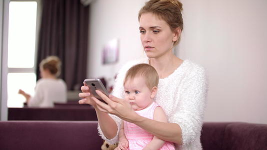妇女在家里用电话工作和照顾孩子视频的预览图
