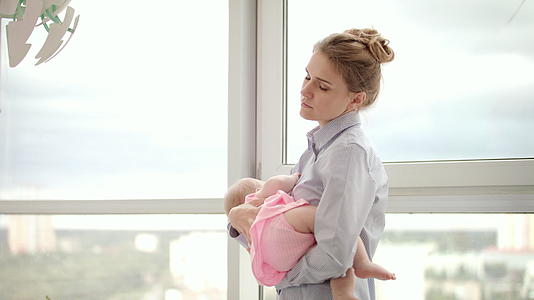 母亲手里拿着婴儿的疲惫母亲靠近窗户视频的预览图
