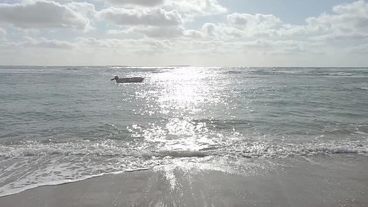 一艘孤立的船在海浪上慢慢地落在岸边太阳反射在后面视频的预览图