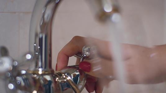 女子用手把水从水龙头转入浴室玻璃杯视频的预览图