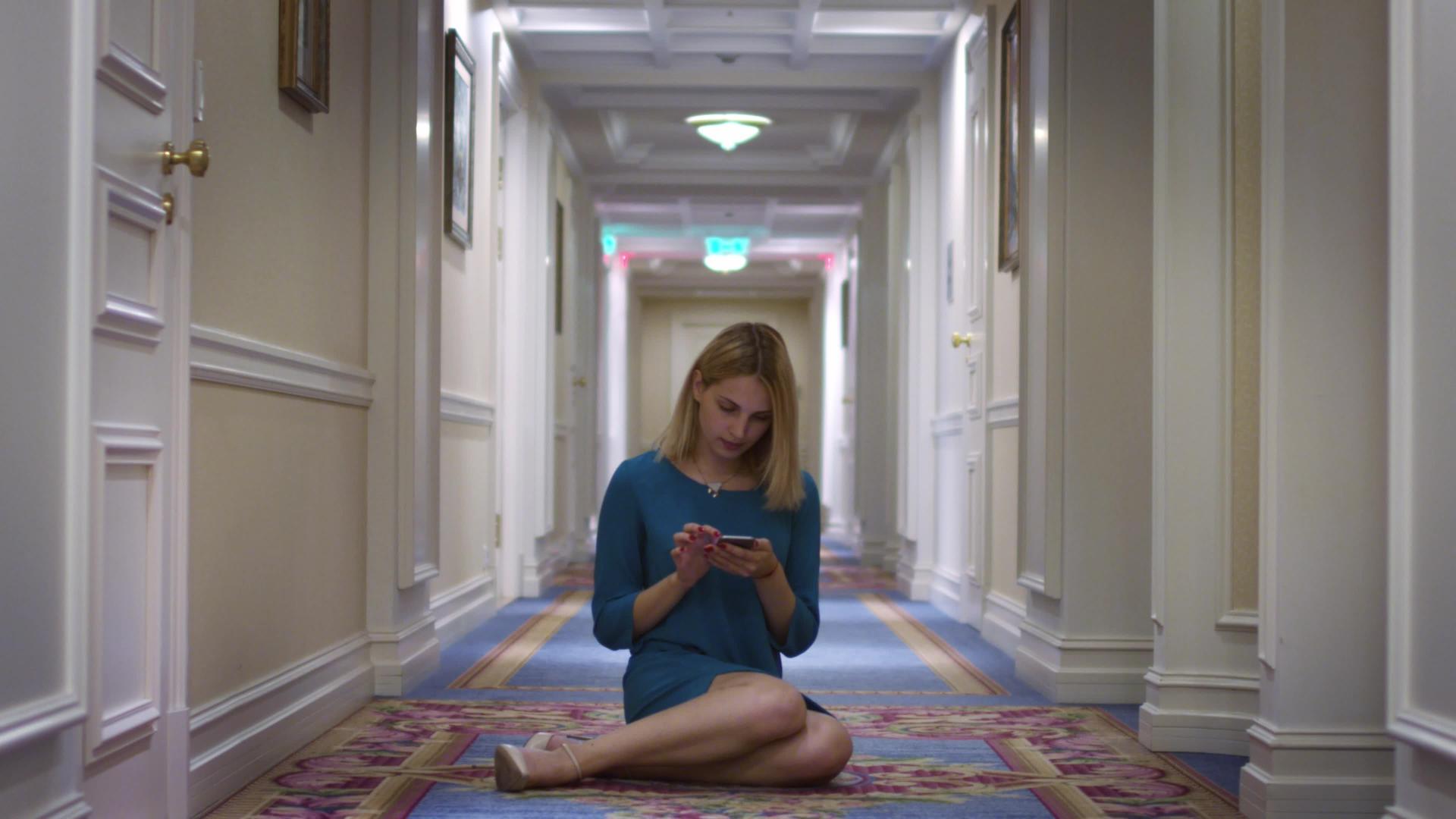年轻女性坐在长长的走廊中间用手机视频的预览图