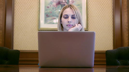 美丽的女人坐在家庭办公室的桌子上看着笔记本屏幕视频的预览图