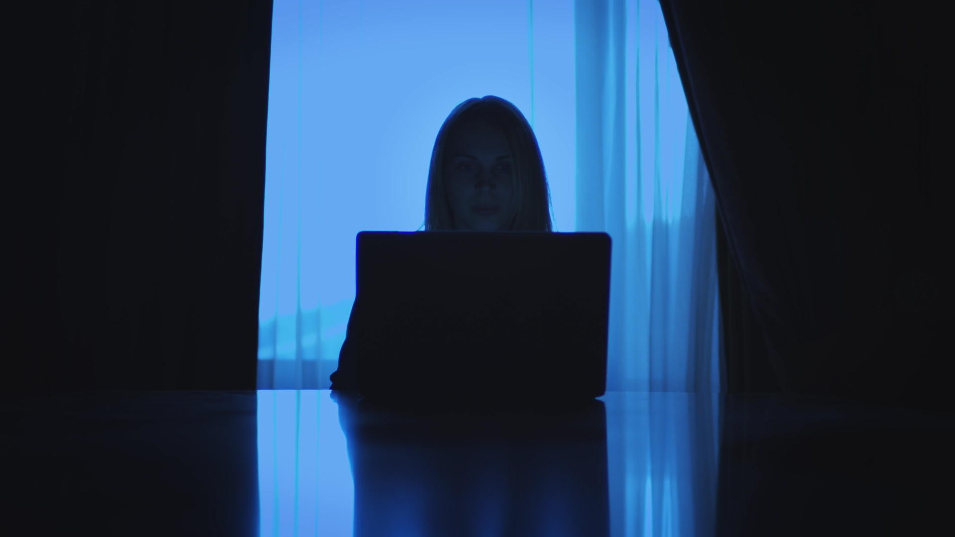 坐在黑暗房间窗口后面的商业女性从事笔记本电脑工作视频的预览图