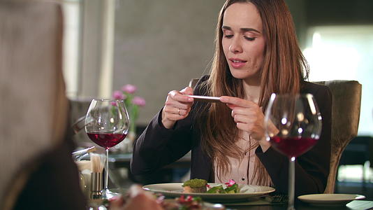 女商人在餐厅的智能手机上拍摄食物照片视频的预览图