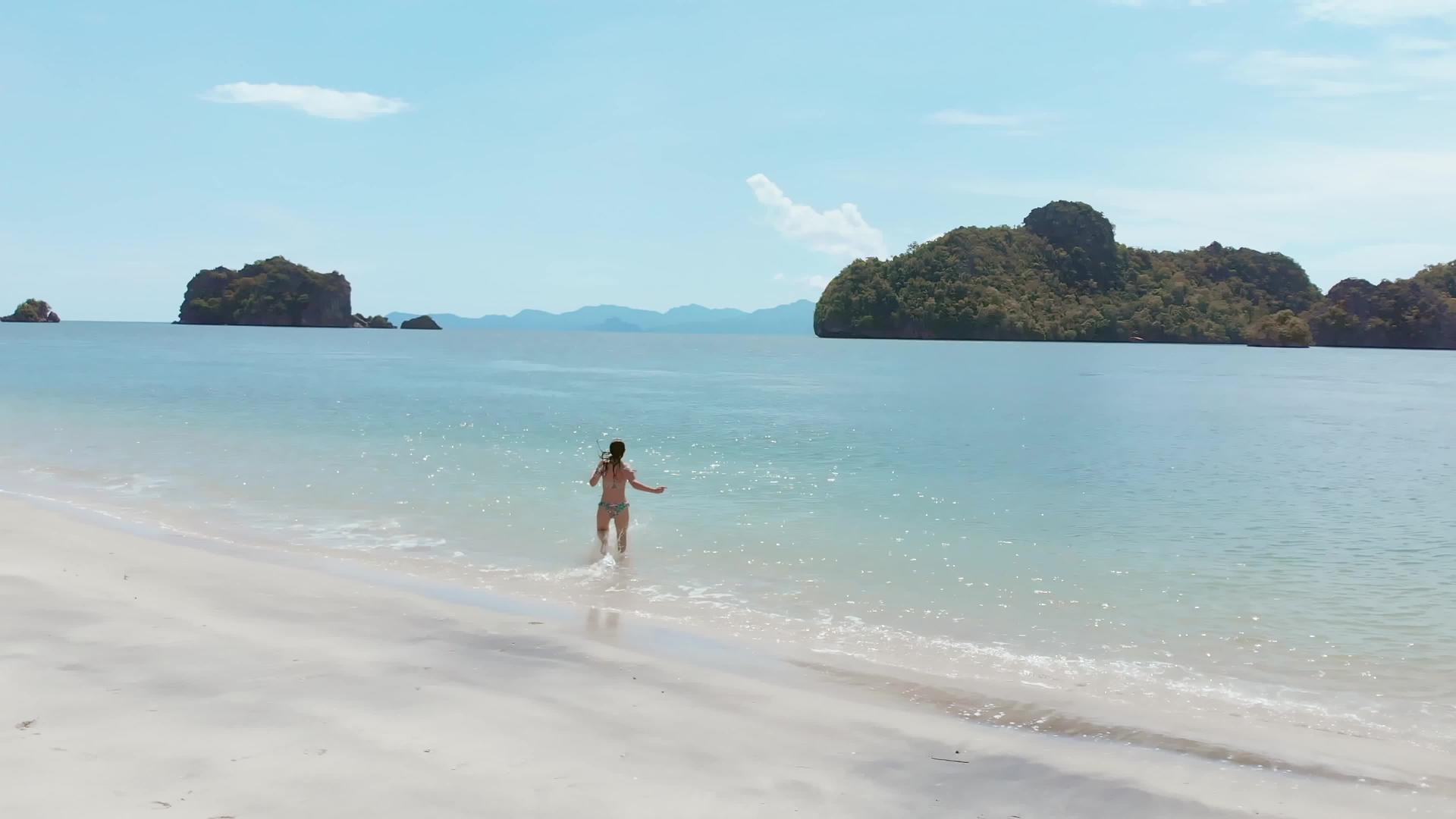 一个穿着泳衣的女孩沿着海滩潜入清澈的热带岛屿视频的预览图