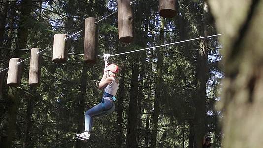 年轻女性在爬树公园的木材之间用绳子在爬树之间移动安全设备视频的预览图