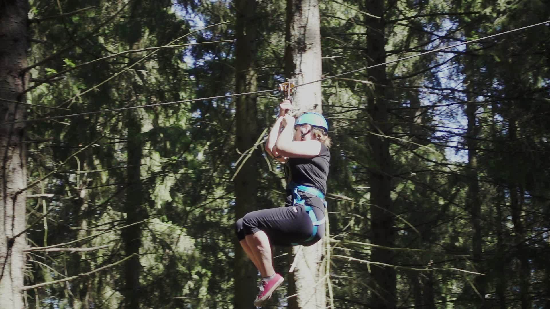 年轻女性戴着保护头盔和腰带在爬树公园用绳子移动视频的预览图