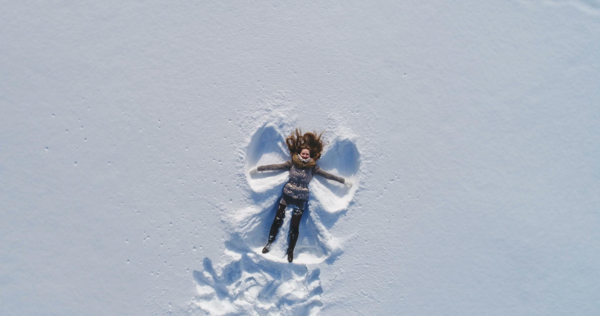 快乐的年轻女性躺在雪地上做着雪天使的慢动作在空中观光和旋转视频的预览图