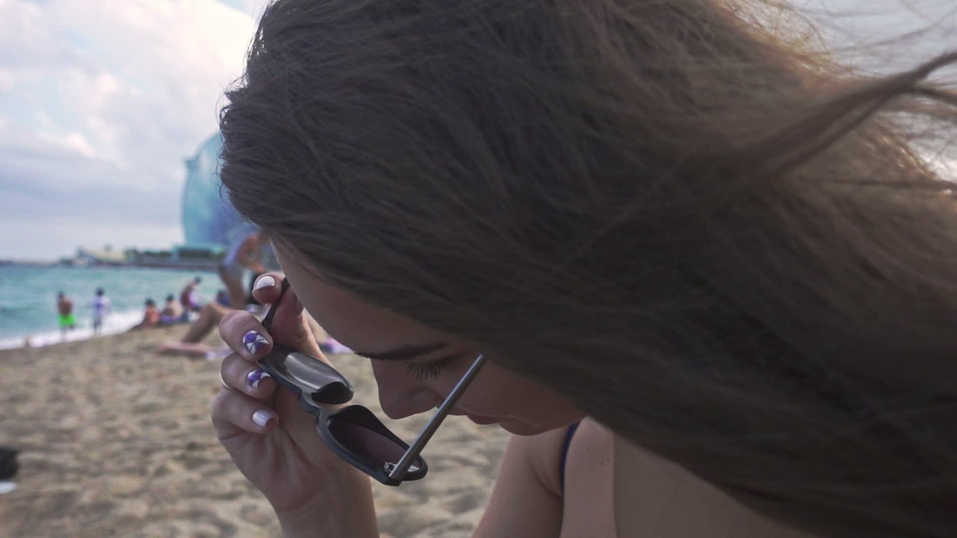 女孩戴着太阳镜坐在沙滩上视频的预览图