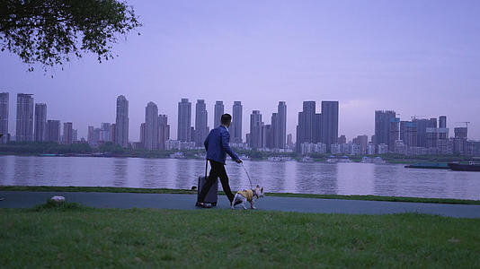 4k素材慢镜头升格拍摄城市江滩街景拖着行李箱遛狗的男人视频的预览图