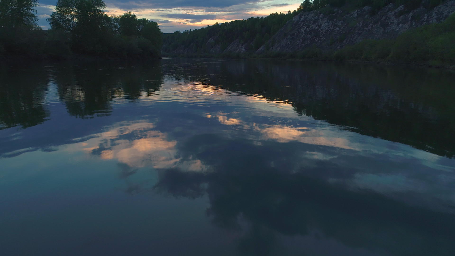 日落时低角迅速飞过河面河边有绿树的岩石和云彩视频的预览图