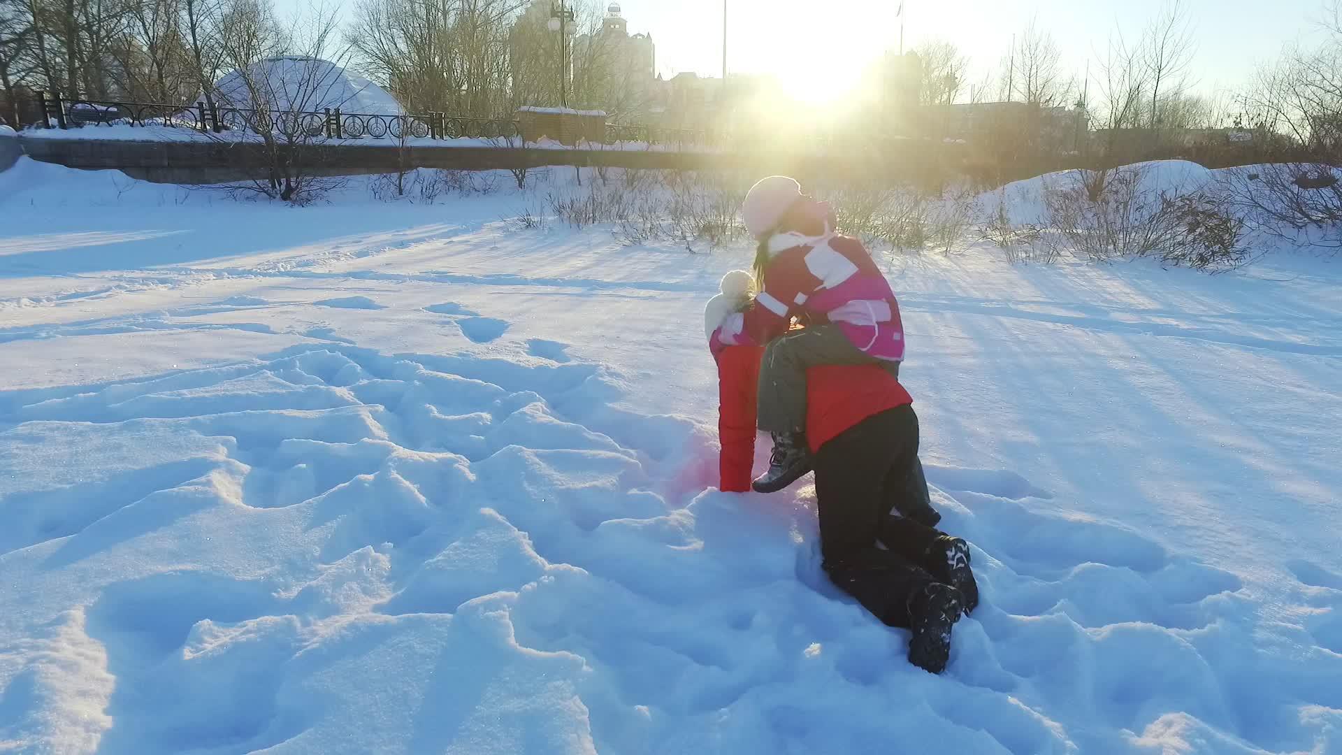 冬天在雪地里快乐快乐的妈妈和女儿在阳光明媚的冬季公园里玩耍视频的预览图