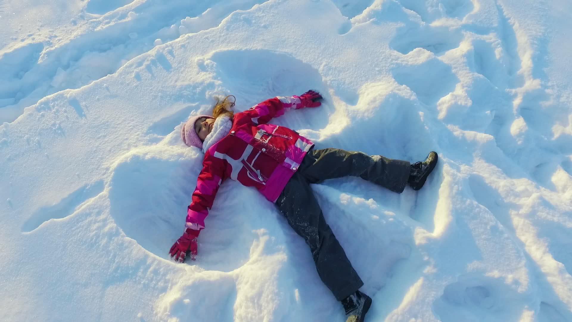 孩子做雪天使美丽的女孩在雪中玩耍视频的预览图