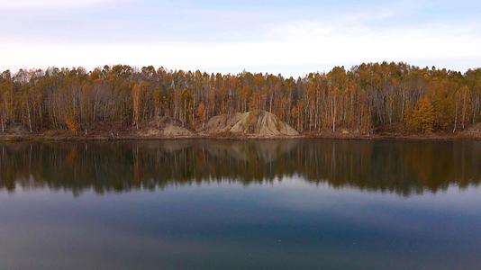 从上面看相机飞过平静美丽的湖面飞向秋天的树木和森林视频的预览图