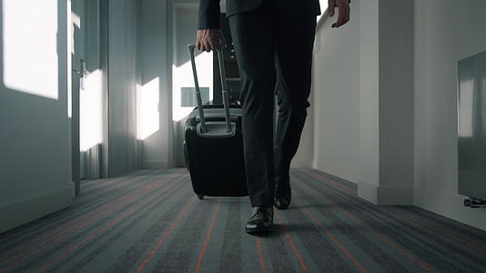 在酒店走廊旅行时带着旅李箱的商腿男视频的预览图