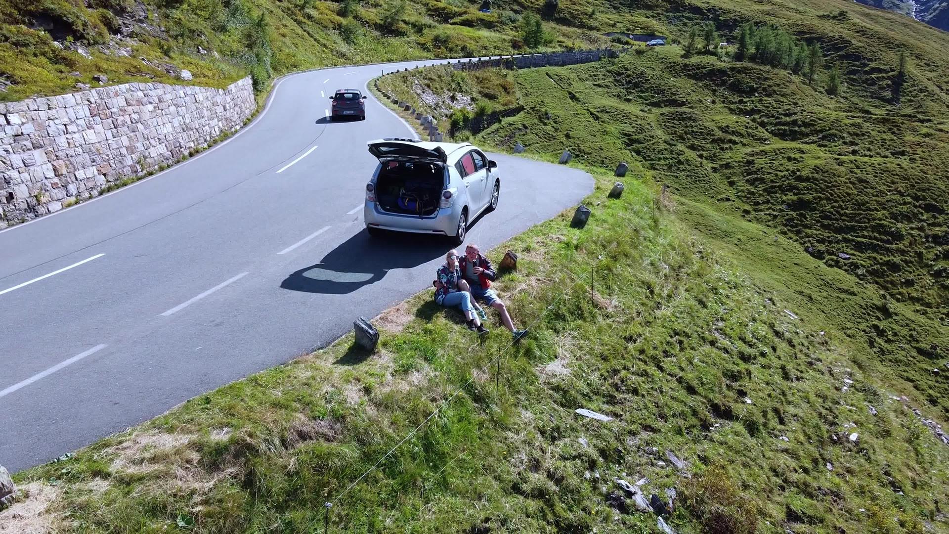 情侣们坐在路附近的山上喝酒观看无人驾驶无人机视频的预览图