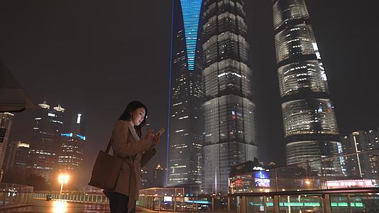 4K秋冬夜晚商务建筑前女性看手机升格100p视频的预览图