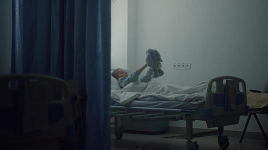生病的女孩独自躺在病床上心烦意乱地玩毛绒玩具视频的预览图