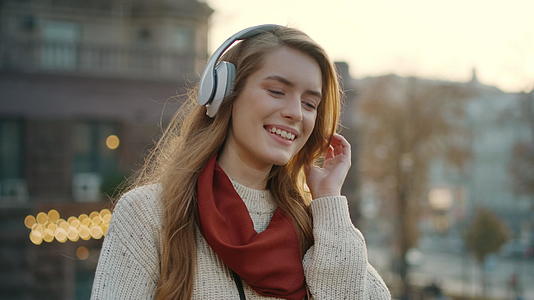 年轻女性在户外用耳机听歌舞视频的预览图