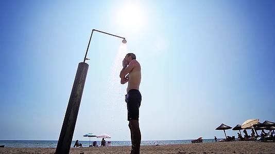 男子在沙滩上洗澡在太阳电影镜头前慢慢洗身体视频的预览图