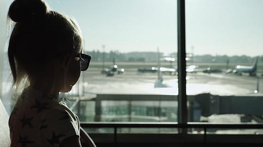 日落时戴着墨镜等待飞机的小女孩坐在机场客运大楼等候区视频的预览图