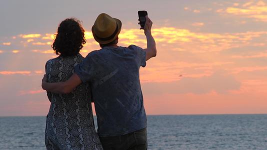 美丽的年轻夫妇在智能手机上寻找日出日落自拍视频的预览图