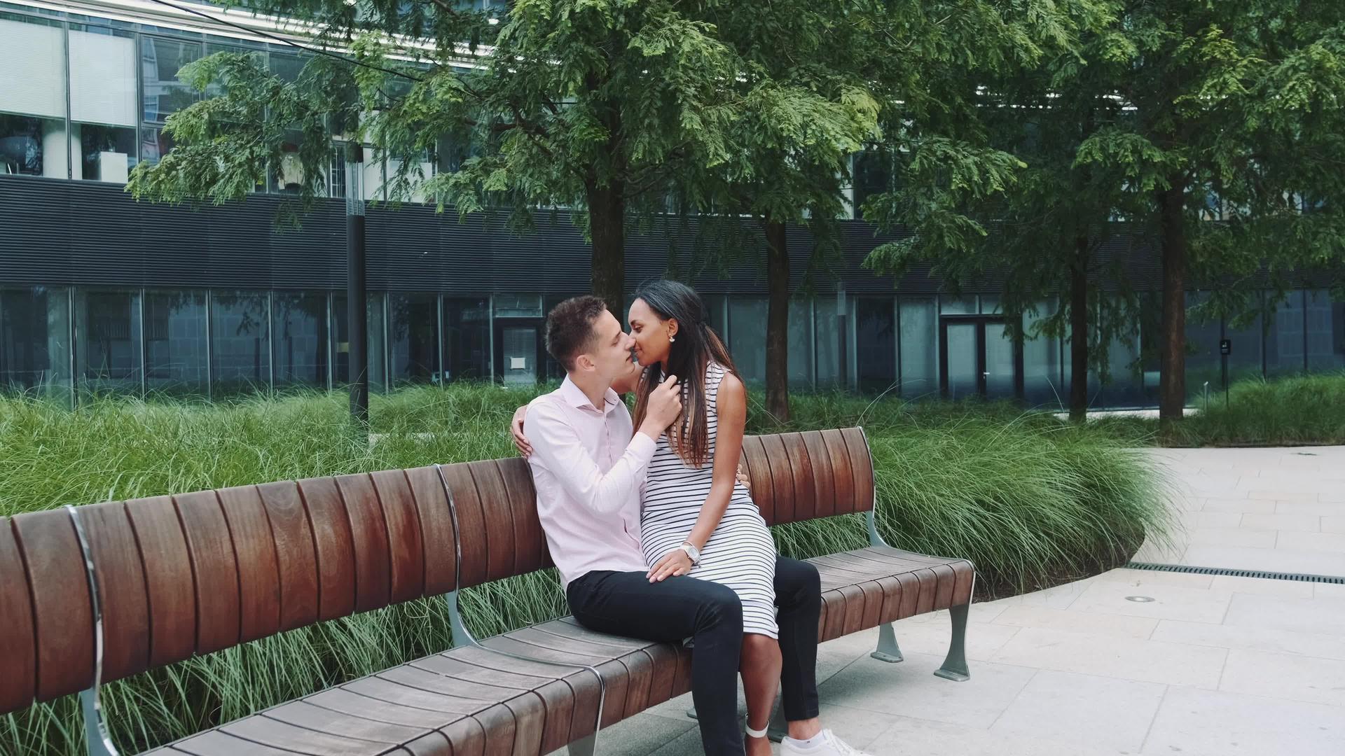 年轻多种族的夫妻坐在长凳上接吻视频的预览图