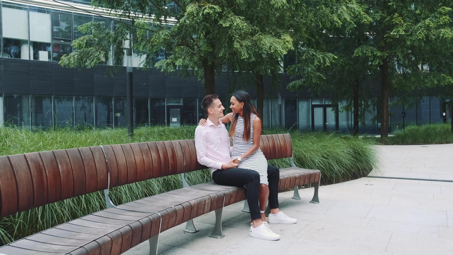 年轻男子亲吻女友的手坐在公园的长椅上视频的预览图