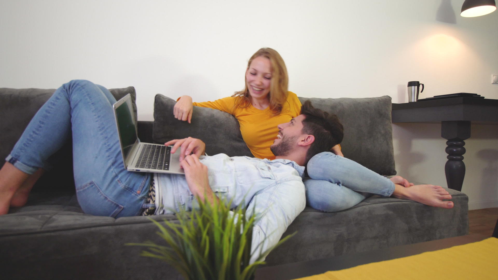 情侣们在沙发上爱着笔记本电脑笑着躺在女孩腿上视频的预览图