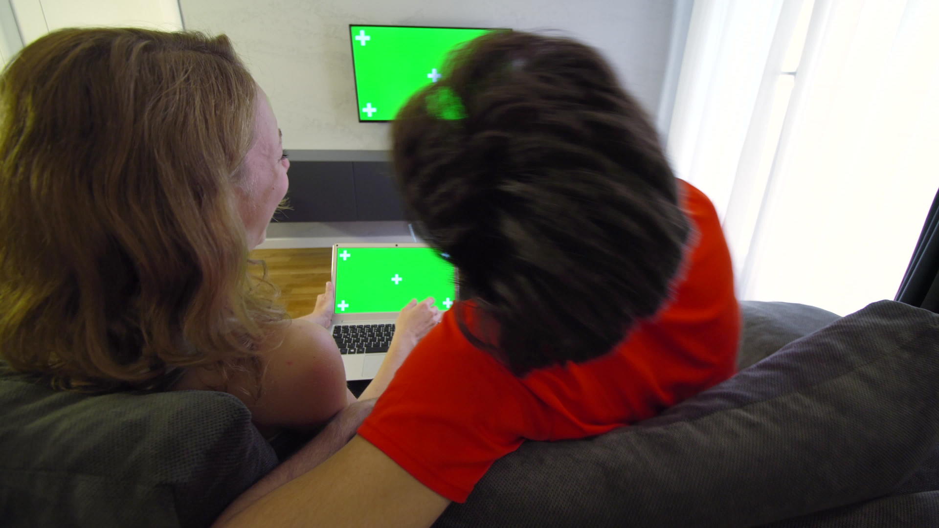 客厅里的一对夫妇使用绿色屏幕笔记本电脑和电视视频的预览图