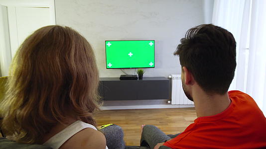 一对夫妇在客厅看电视绿屏关注人们视频的预览图