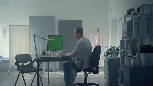 医院办公室的医生使用绿屏电脑在线咨询患者视频的预览图