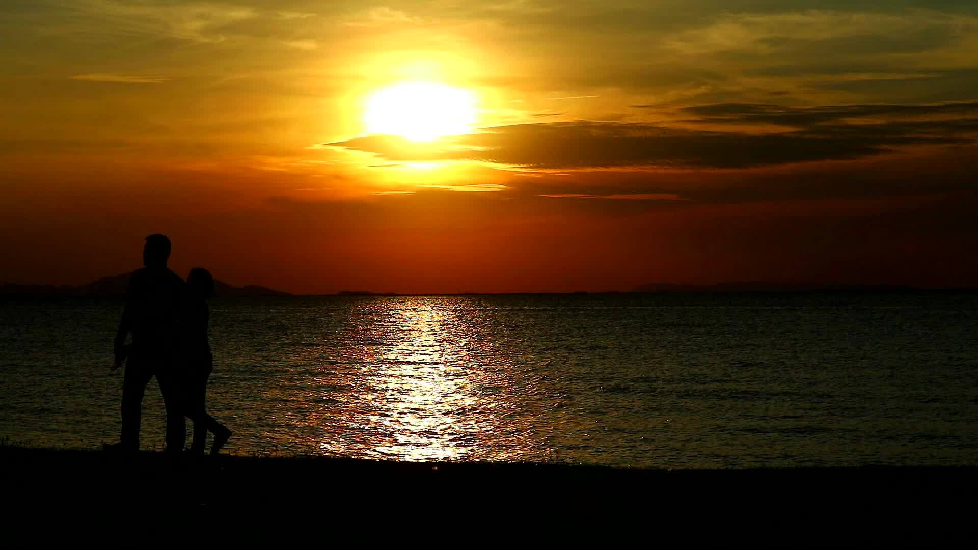 这对夫妇在海边日落时在海滩上散步视频的预览图