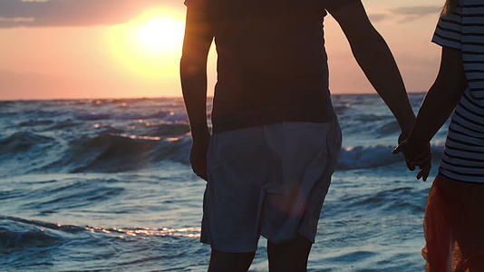 一对夫妇在日落时用粗糙的大海握手视频的预览图