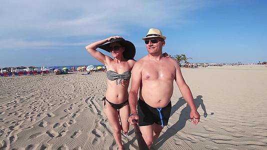 一对穿着比基尼和帽子的夫妇在热带海滩上散步视频的预览图
