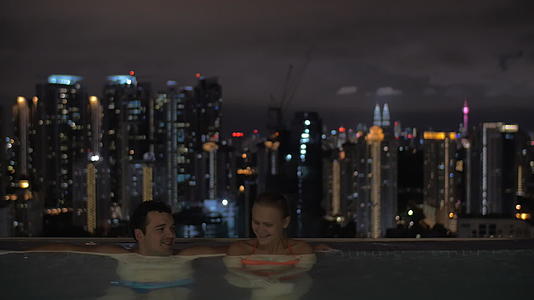 晚上我看到年轻漂亮的情侣在屋顶的游泳池里露天看到城市视频的预览图